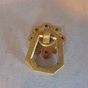 May include: A vintage brass drawer pull with a floral backplate and a geometric handle. The hardware is a warm gold color, showing signs of age and use. The pull is designed for furniture restoration or decorative purposes.