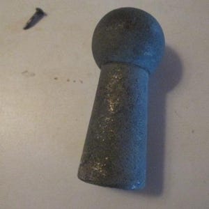 May include: A gray bottle stopper with a rounded top and a conical body. The stopper has a textured surface and appears to be made of stone or a similar material. The object is set against a plain, off-white background.