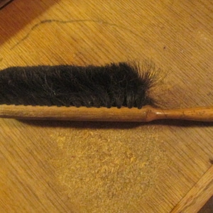May include: A wooden-handled brush with black bristles. The brush is made of natural materials and has a simple design.