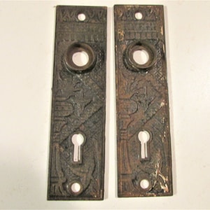 May include: A pair of antique door plates with intricate designs. The plates are made of metal and have a dark brown finish. Each plate has a keyhole and a round knob hole.