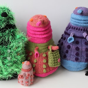 Könnte beinhalten: Vier gestrickte Plüschtiere in verschiedenen Farben und Stilen. Die Spielzeuge stehen alle aufrecht und haben verschiedene Texturen.