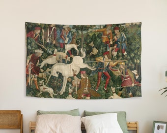 May include: A tapestry depicting a scene of a unicorn hunt. The unicorn is white and is being chased by a group of hunters on horseback. The tapestry is framed in a wooden frame and is hanging on a white wall.