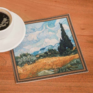 Puede incluir: Un posavasos cuadrado con una imagen enmarcada de una pintura de paisaje. La pintura representa un campo de trigo con un alto cipr&eacute;s en el fondo. El cielo es azul con nubes blancas. El posavasos tiene un marco de madera marr&oacute;n.