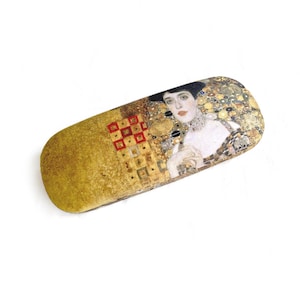May include: A rectangular eyeglasses case featuring a portion of a Gustav Klimt painting. The case has a gold-colored textured base with a section of the painting depicting a woman with a decorative collar and a dark hat.
