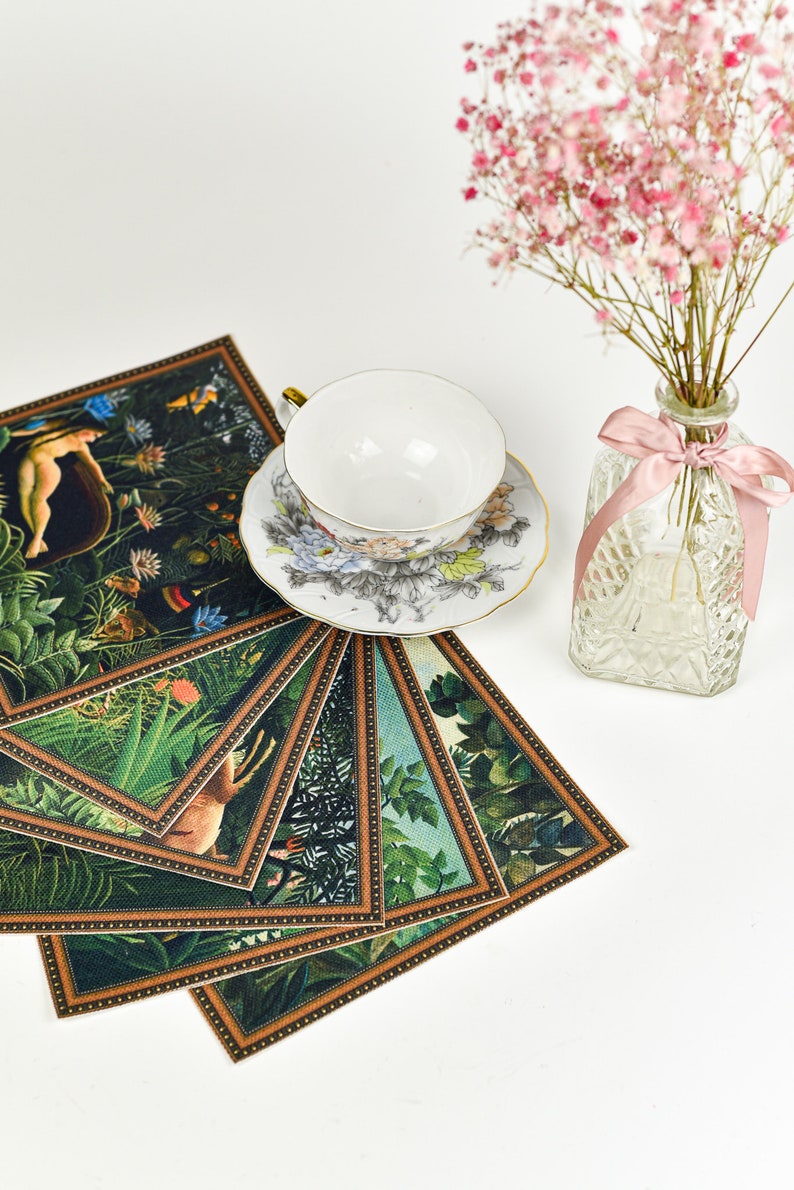 Puede incluir: Una taza y un platillo blancos con dise&ntilde;os florales se asientan sobre una pila de posavasos decorativos con escenas de la jungla. Tambi&eacute;n hay un peque&ntilde;o jarr&oacute;n de cristal con flores rosas y una cinta rosa.