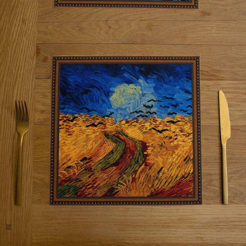 May include: A brown wooden table setting with a placemat featuring a painting of a field with a winding path and a blue sky. The painting is framed with a brown border. A gold fork and knife are placed on the table.
