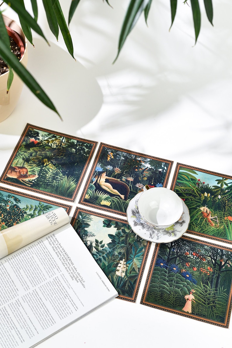 Puede incluir: Un juego de seis manteles individuales cuadrados con ilustraciones de tem&aacute;tica selv&aacute;tica y bordes marrones. Una taza y un platillo blancos est&aacute;n encima. La obra de arte representa figuras, plantas y animales. Tambi&eacute;n se ve una revista.
