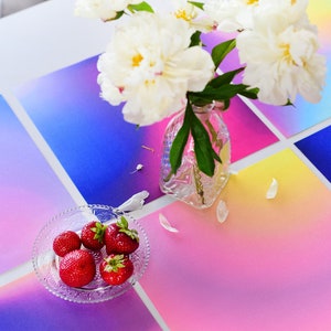 May include: A white table setting with a bouquet of white peonies in a clear glass vase. The table is set with colorful gradient placemats and a small glass bowl of fresh strawberries.