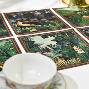 Puede incluir: Una taza y un platillo blancos con dise&ntilde;os florales se encuentran cerca de un mantel individual decorativo con escenas de la jungla. Tambi&eacute;n es visible un servilletero dorado. El mantel individual tiene un borde marr&oacute;n y representa exuberante follaje verde y figuras.