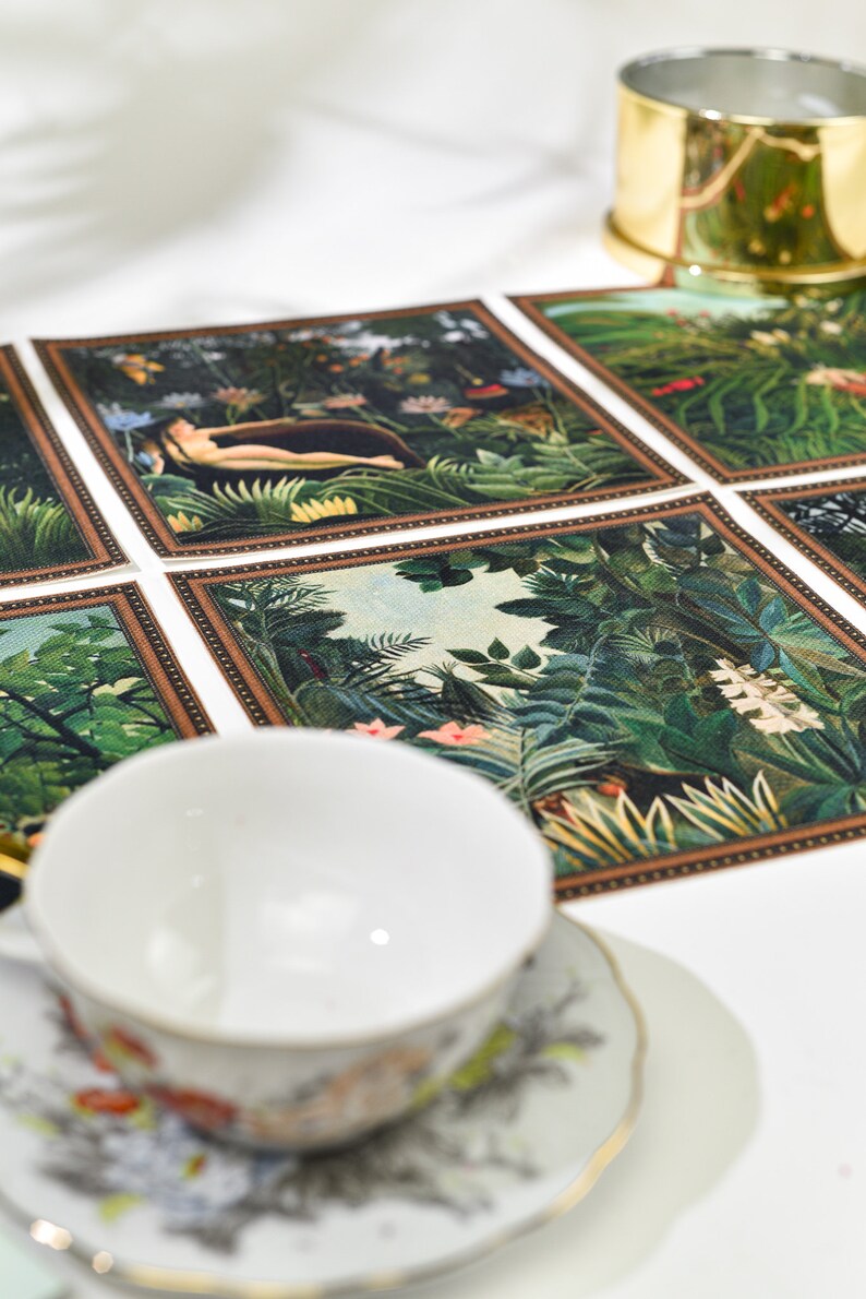 Puede incluir: Una taza y un platillo blancos con dise&ntilde;os florales se encuentran cerca de un mantel individual decorativo con escenas de la jungla. Tambi&eacute;n es visible un servilletero dorado. El mantel individual tiene un borde marr&oacute;n y representa exuberante follaje verde y figuras.