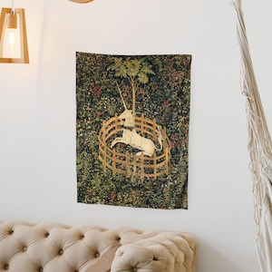 May include: A tapestry depicting a white unicorn trapped in a circular fence, surrounded by a lush green forest with red berries and flowers. The unicorn is facing right and has a golden horn.