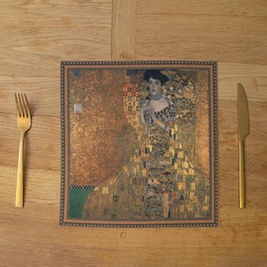 May include: A gold and brown placemat with a framed image of a woman in a gold dress. The image is a mosaic of small squares and rectangles, creating a textured effect.