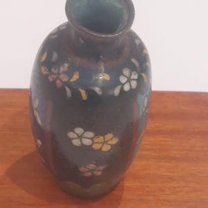 May include: A small, black, oval-shaped vase with a floral design. The vase is decorated with white, pink, and yellow flowers.