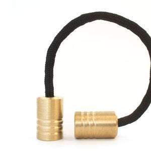 May include: Two gold-colored metal beads with a black cord threaded through them. The beads have a ridged design.