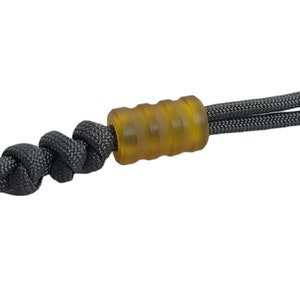 May include: A black paracord lanyard with a yellow plastic bead. The bead has a ridged texture.