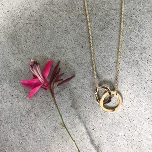 May include: A gold chain necklace with a double circle pendant. The pendant is made of two interlocking circles.
