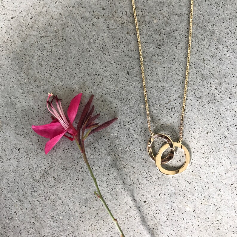 May include: A gold chain necklace with a double circle pendant. The pendant is made of two interlocking circles.