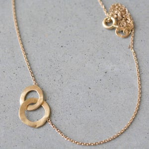 May include: A gold chain necklace with a pendant featuring two interlocking circles.
