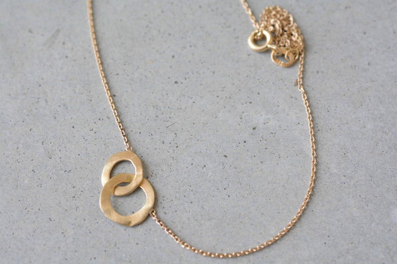 May include: A gold chain necklace with a pendant featuring two interlocking circles.