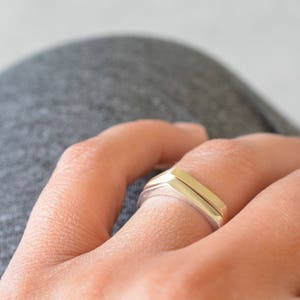 May include: A silver ring with a geometric design. The ring is worn on a finger.