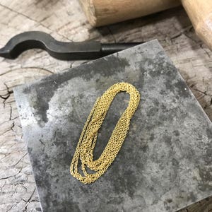 May include: A gold chain necklace on a gray metal surface. The chain is made of small, linked circles.