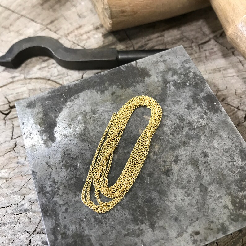 May include: A gold chain necklace on a gray metal surface. The chain is made of small, linked circles.
