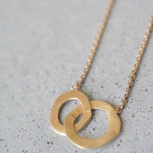 May include: A gold necklace with a double circle pendant. The circles are interlocked and have a slightly hammered texture.