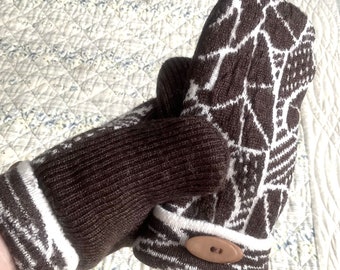 May include: A pair of brown and white knitted mittens. The mittens have a geometric pattern in white against a brown background. The cuffs are brown with white stripes. A wooden button secures the cuff. The mittens are designed for warmth and style.