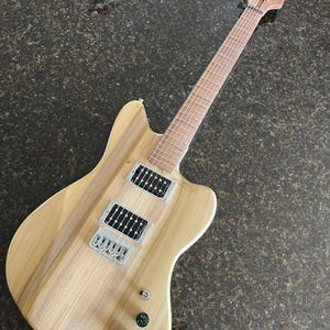 Puede incluir: Una guitarra el&eacute;ctrica con cuerpo de madera clara de veta natural, m&aacute;stil y diapas&oacute;n de arce. Cuenta con dos pastillas humbucker negras, un puente plateado, tres perillas de control y un clavijero con la marca Glarry impresa en negro.