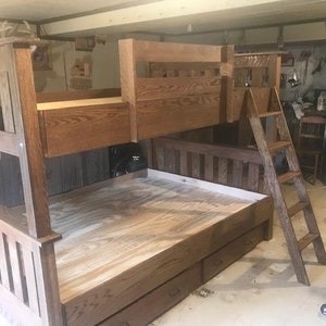 May include: A wooden bunk bed with a ladder. The bed frame is made of light brown wood and has a simple design. The top bunk is accessible by a wooden ladder. The bottom bunk has two drawers.