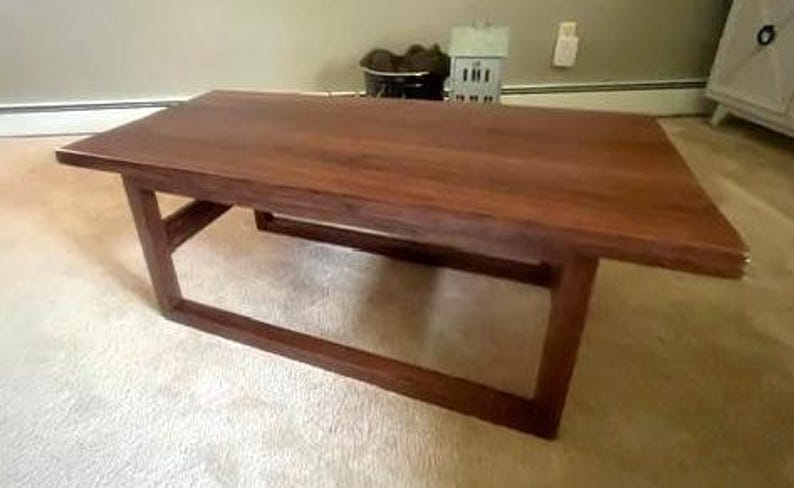 May include: A rectangular coffee table constructed from dark brown wood. The table features a smooth, flat top surface and a base composed of four vertical legs connected by horizontal support bars, creating an open, geometric frame design.