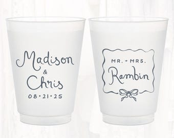 May include: Two white plastic cups with black text. One cup says "Madison & Chris 08.21.25". The other cup says "Mr. & Mrs. Rambin" with a decorative bow.