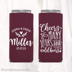 May include: Two maroon can coolers with white text. One cooler says "Jenna & Drew Miller 07.07.23" with a heart and floral design. The other cooler says "Cheers to many years and cold beers" with a heart.