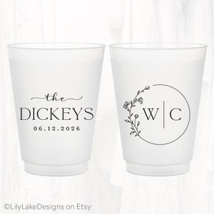 Pu&ograve; includere: Due bicchieri in plastica satinata con disegni stampati in nero. Un bicchiere mostra il testo the DICKEYS e la data 06.12.2026. L'altro presenta una cornice circolare con un ramo floreale sul lato sinistro e le lettere W e C separate.