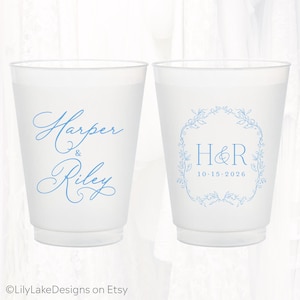 May include: Two frosted plastic cups featuring light blue ink. The left cup displays the names Harper & Riley in a cursive script. The right cup features the initials H&R inside a floral wreath with the date 10-15-2026 printed below.