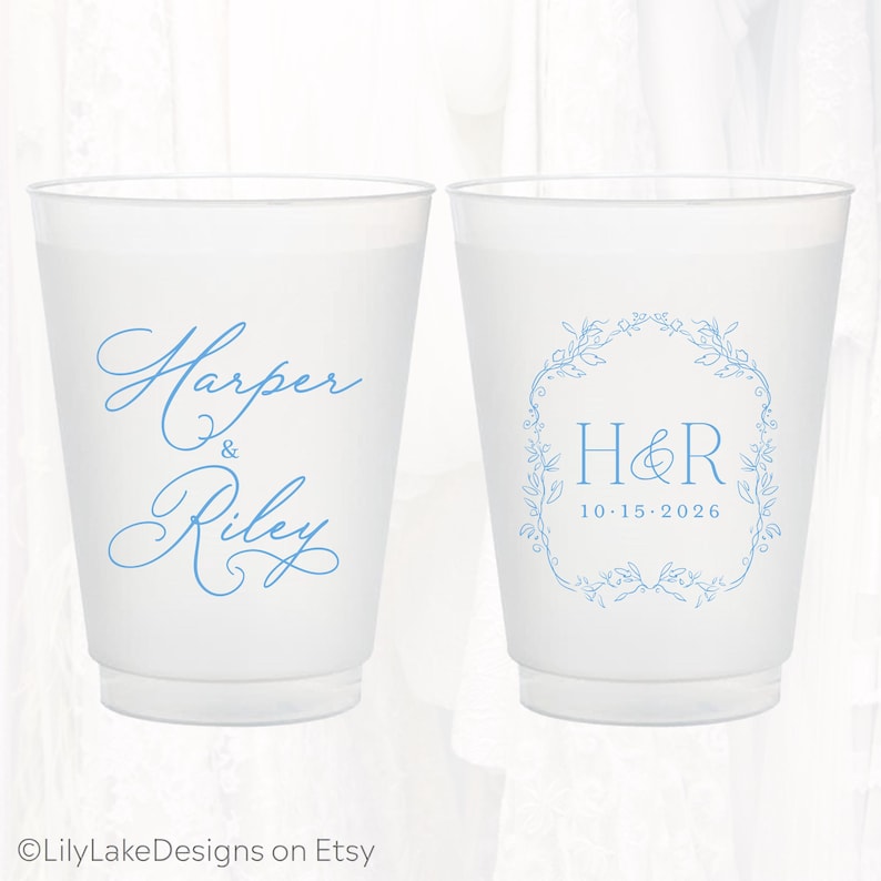 May include: Two frosted plastic cups featuring light blue ink. The left cup displays the names Harper & Riley in a cursive script. The right cup features the initials H&R inside a floral wreath with the date 10-15-2026 printed below.