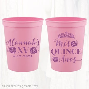 May include: Two pink plastic cups with purple text and designs. One cup says "Alannah's XV 4.12.2024" and the other says "Mis Quince A&ntilde;os" with a crown design.