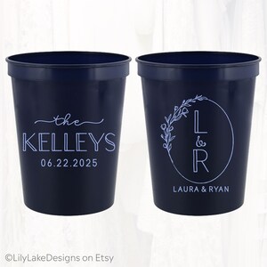 May include: Two navy blue plastic cups with white text. One cup says "the Kelleys 06.22.2025". The other cup has a floral wreath with the letters "L & R" inside and the text "Laura & Ryan" below.