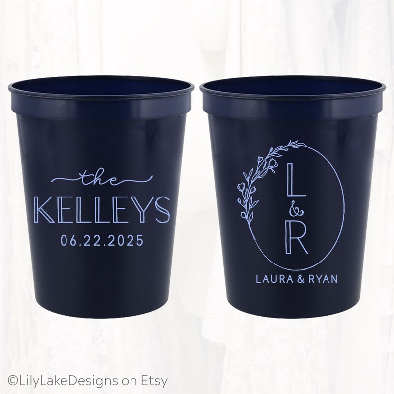 May include: Two navy blue plastic cups with white text. One cup says "the Kelleys 06.22.2025". The other cup has a floral wreath with the letters "L & R" inside and the text "Laura & Ryan" below.