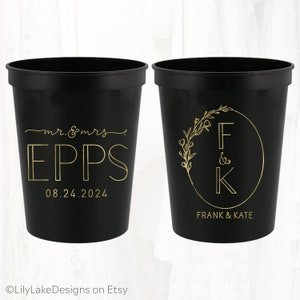 May include: Two black plastic cups with gold lettering. One cup says "mr. & mrs. EPPS 08.24.2024". The other cup has a floral design with the letters "F & K" inside a circle and the text "FRANK & KATE" below.