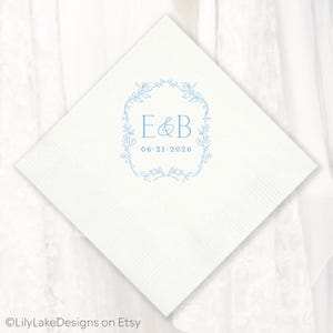 Puede incluir: Servilleta de papel cuadrada blanca con un dise&ntilde;o floral azul claro y las iniciales "E&B" junto con la fecha "06.21.2026". La servilleta tiene una superficie texturizada, ideal para una boda o evento especial.