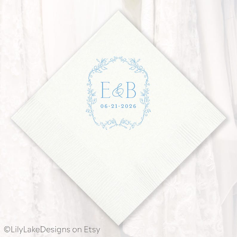 Puede incluir: Servilleta de papel cuadrada blanca con un dise&ntilde;o floral azul claro y las iniciales "E&B" junto con la fecha "06.21.2026". La servilleta tiene una superficie texturizada, ideal para una boda o evento especial.