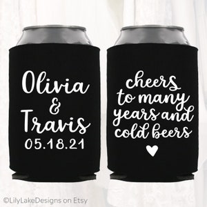 May include: Two black can coolers with white text. One cooler says "Olivia & Travis 05.18.21". The other cooler says "Cheers to many years and cold beers" with a white heart.