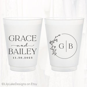 Pu&ograve; includere: Due bicchieri in plastica satinata con testo e grafiche stampate in nero. Un bicchiere mostra i nomi GRACE e BAILEY con la data 11.30.2023. L'altro bicchiere presenta un disegno a corona floreale circolare attorno alle iniziali G e B.