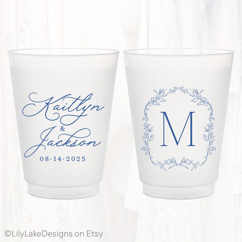 May include: Two frosted plastic cups featuring blue ink designs. The left cup displays the names Kaitlyn & Jackson with the date 08.14.2025 in script and serif fonts. The right cup features a large letter M inside a blue floral wreath design.
