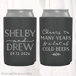 May include: Two black and gray can coolers. One cooler says "Shelby and Drew 09.12.2026". The other cooler says "Cheers to many years & a lot of cold beers".
