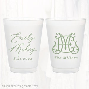 May include: Two white plastic cups with green text and designs. One cup says "Emily & Mikey 8.21.2024" and the other cup has a green monogram and says "The Millers".