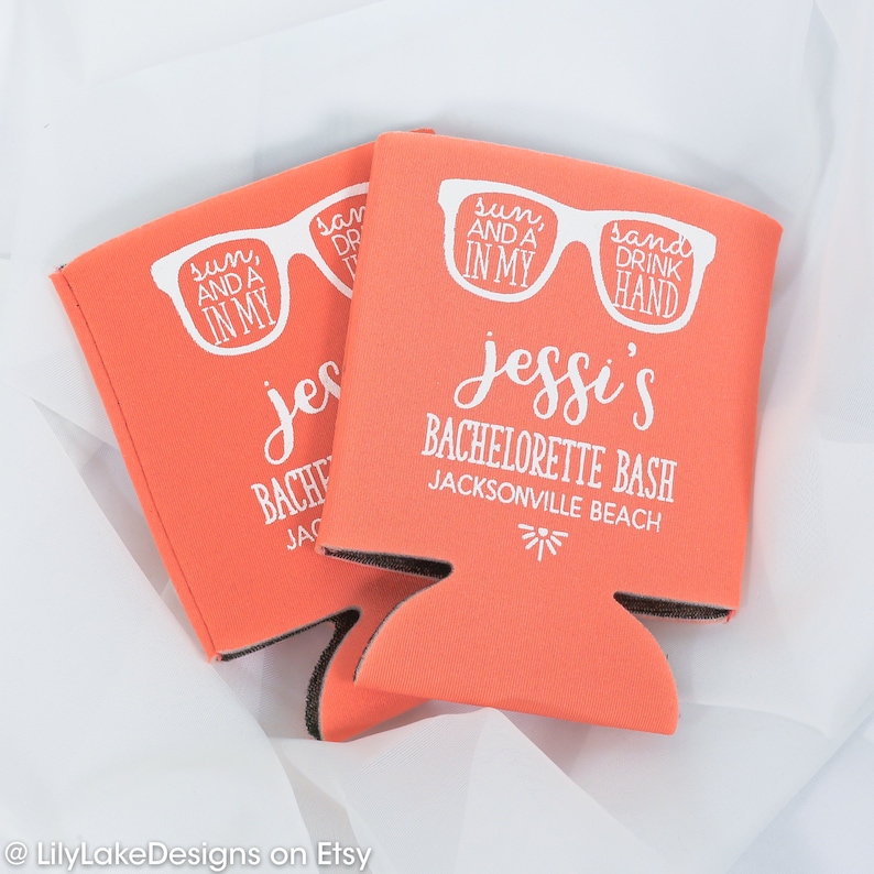 K&ouml;nnte beinhalten: Zwei korallenorange Schaumstoff-Getr&auml;nkedosenk&uuml;hler mit wei&szlig;em Text und einer Grafik von Sonnenbrillen. Der Text lautet "sun, and a drink in my hand" und "Jessi's Bachelorette Bash Jacksonville Beach".