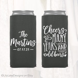 May include: Two black and grey can coolers. One cooler has the text "The Martins - 07.17.21 -" printed on it. The other cooler has the text "Cheers to many years and cold beers" printed on it.