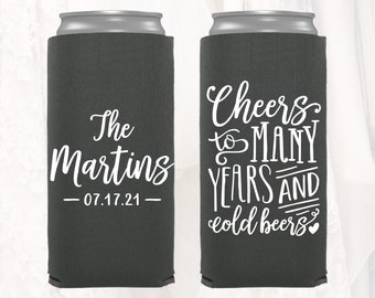 May include: Two dark gray can coolers with white text. One says "The Martins - 07.17.21" and the other says "Cheers to MANY YEARS AND cold beers" with a heart. The coolers are designed to keep beverages cold.